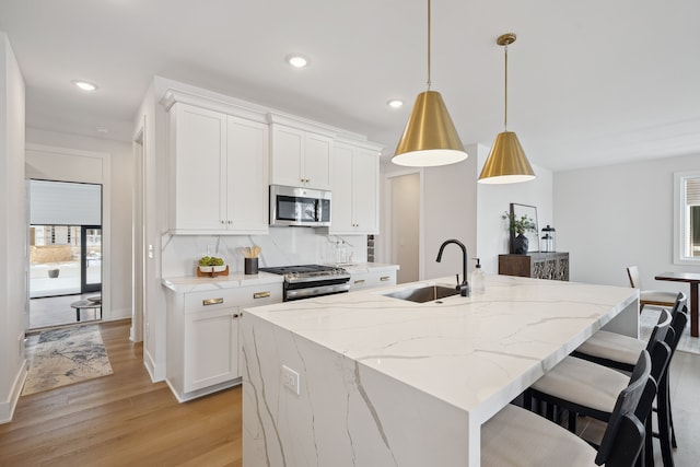 kitchen with appliances with stainless steel finishes, an island with sink, decorative light fixtures, and white cabinets