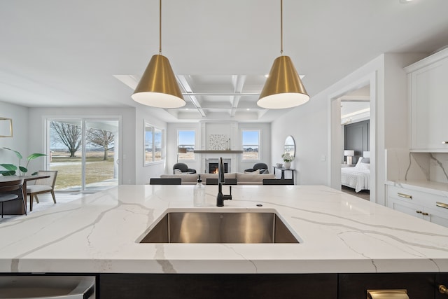 kitchen with white cabinets, light stone counters, open floor plan, decorative light fixtures, and a sink