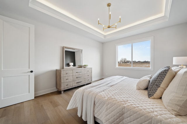 bedroom featuring light wood-style floors, a tray ceiling, and an inviting chandelier