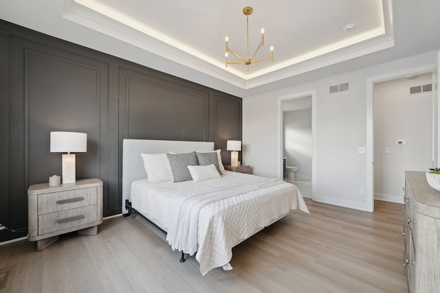 bedroom with a chandelier, light wood-type flooring, a raised ceiling, and visible vents