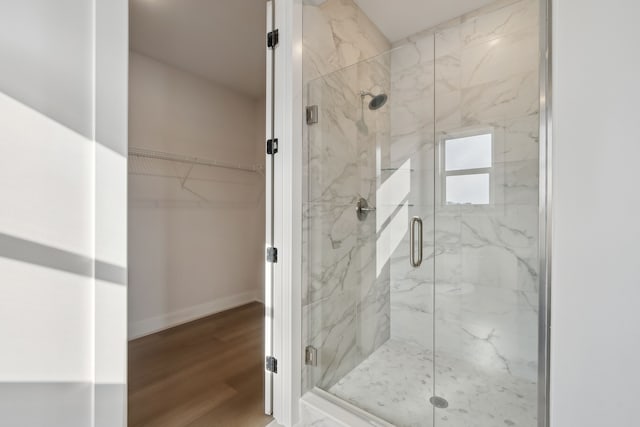 bathroom featuring a marble finish shower, a spacious closet, baseboards, and wood finished floors