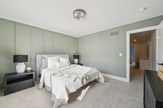 bedroom with light colored carpet, visible vents, a decorative wall, and baseboards