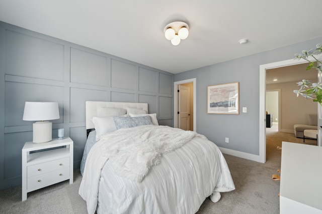 bedroom featuring baseboards, a decorative wall, and light colored carpet