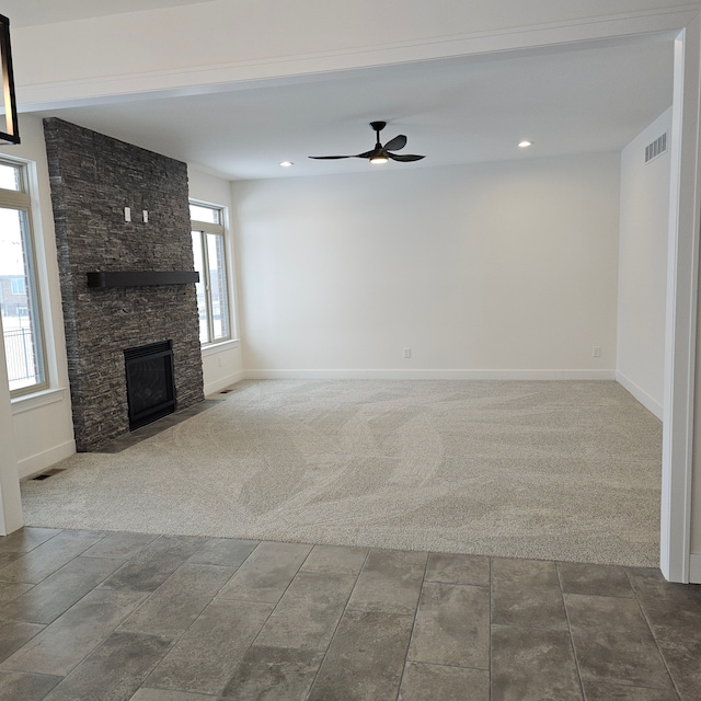 unfurnished living room featuring a stone fireplace, plenty of natural light, ceiling fan, and carpet