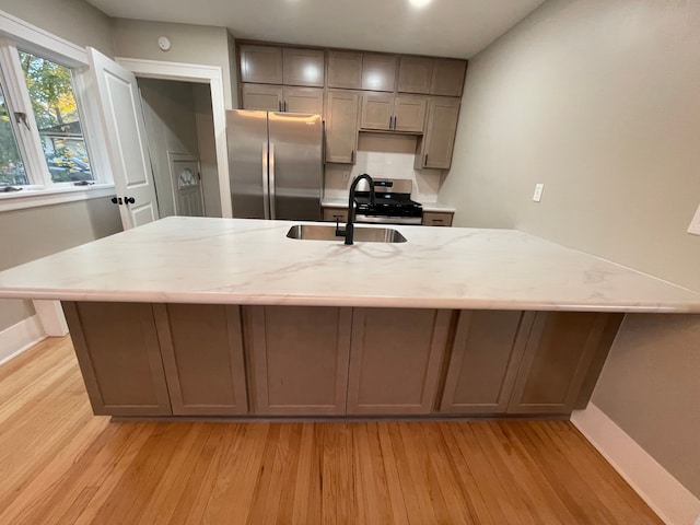 kitchen featuring light wood-type flooring, light stone counters, gray cabinetry, stainless steel appliances, and sink