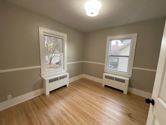 spare room featuring radiator heating unit, light hardwood / wood-style flooring, and plenty of natural light