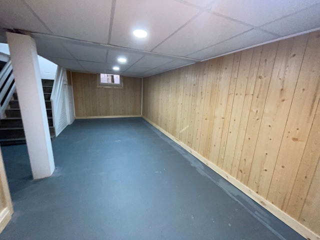 basement with a drop ceiling and wood walls