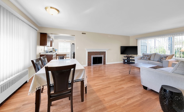 dining area with light wood-type flooring, radiator, and a brick fireplace