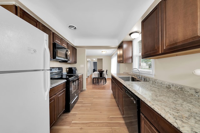 kitchen featuring black appliances, sink, light wood-type flooring, dark brown cabinets, and light stone counters