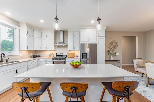 kitchen featuring wall chimney range hood, sink, a kitchen island, white cabinetry, and stainless steel appliances