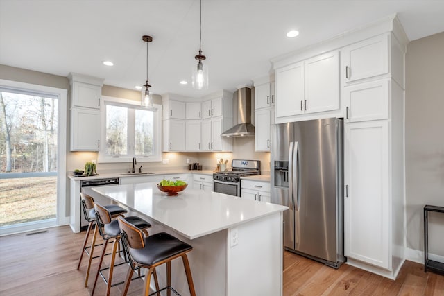 kitchen featuring white cabinetry, a kitchen island, wall chimney range hood, and stainless steel appliances