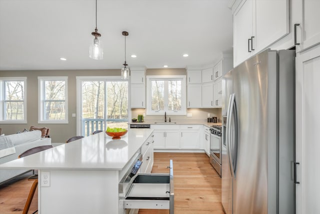 kitchen with a kitchen bar, appliances with stainless steel finishes, decorative light fixtures, a center island, and white cabinetry