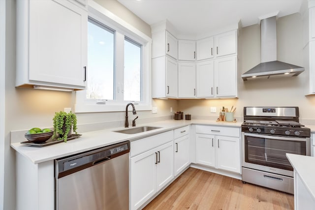 kitchen with white cabinets, sink, light hardwood / wood-style flooring, wall chimney exhaust hood, and stainless steel appliances