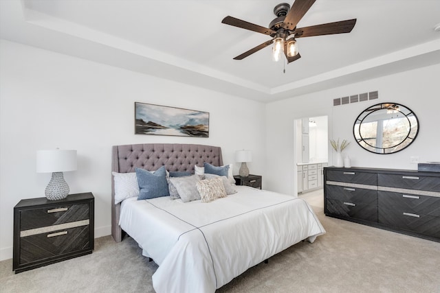 carpeted bedroom featuring ceiling fan, connected bathroom, and a tray ceiling