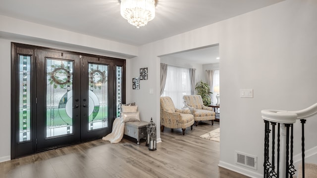 foyer entrance featuring wood-type flooring, french doors, and a chandelier