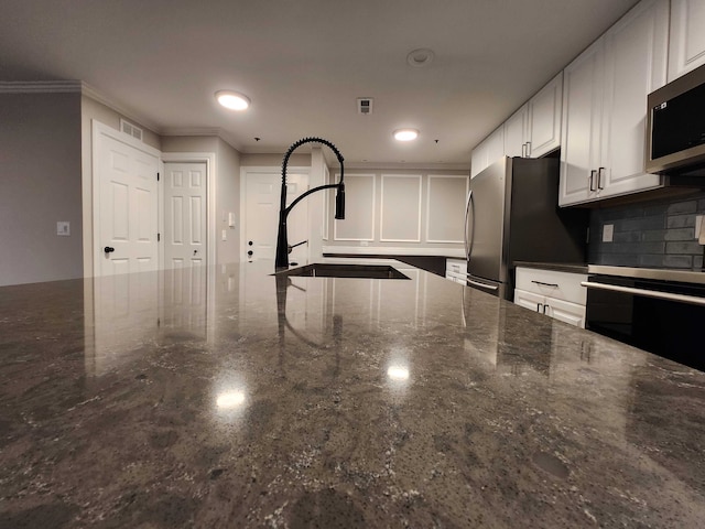 kitchen with sink, dark stone countertops, ornamental molding, appliances with stainless steel finishes, and white cabinetry