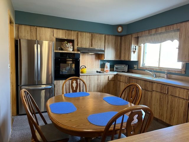 kitchen with exhaust hood, sink, stainless steel fridge, black oven, and cooktop