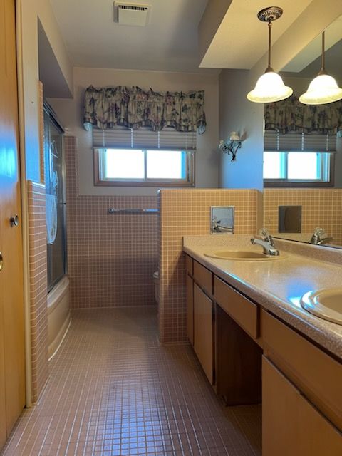 full bathroom with a healthy amount of sunlight, combined bath / shower with glass door, and tile walls