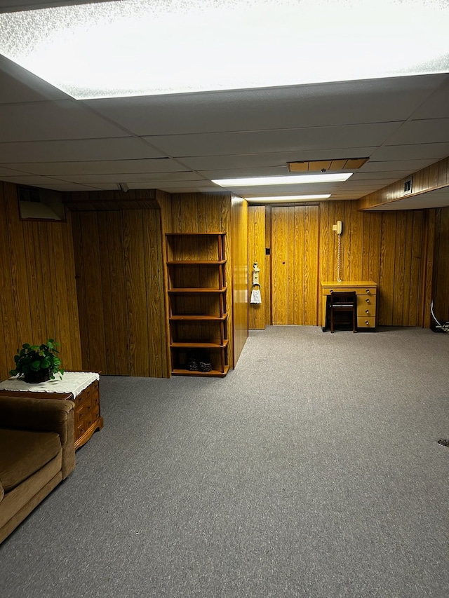 basement with carpet, a paneled ceiling, and wooden walls