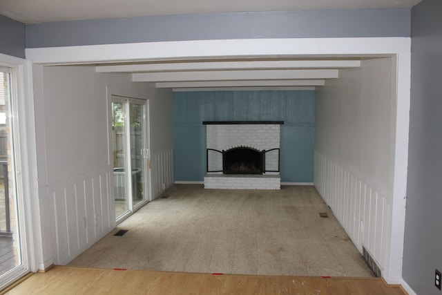 unfurnished living room with a fireplace, hardwood / wood-style floors, beamed ceiling, and a healthy amount of sunlight