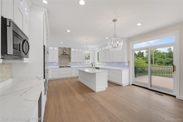 5245 Buell Dr, Commerce Twp, MI 48382 - kitchen with stainless steel microwave, a chandelier, wall chimney exhaust hood, backsplash, and black stovetop