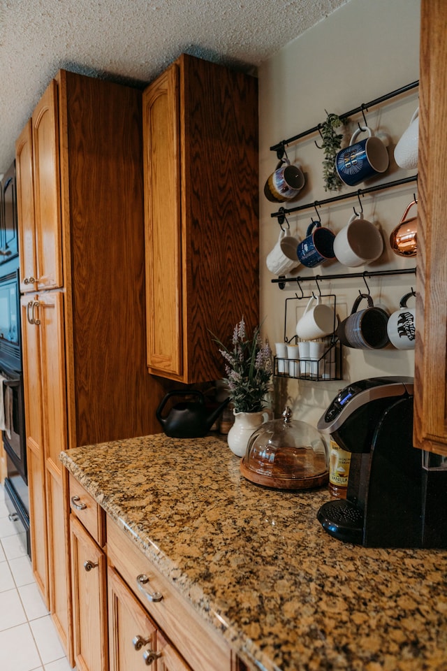 kitchen featuring light stone countertops, a textured ceiling, black oven, and light tile patterned floors