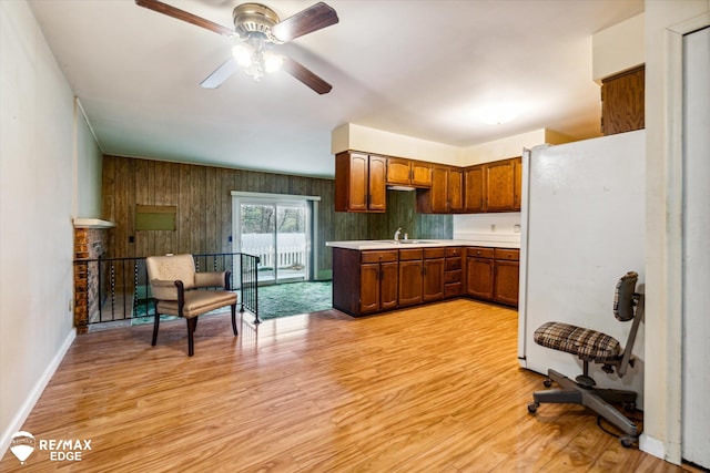 kitchen with ceiling fan, wooden walls, white fridge, and light wood-type flooring