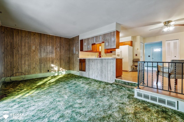 kitchen with dark carpet, white refrigerator with ice dispenser, wooden walls, ceiling fan, and kitchen peninsula