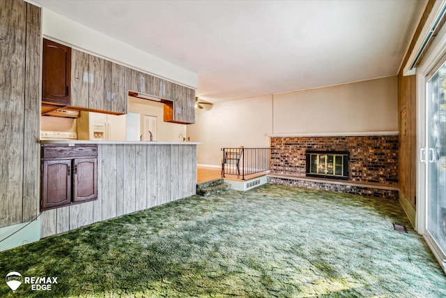 kitchen with carpet flooring, kitchen peninsula, wooden walls, sink, and a fireplace