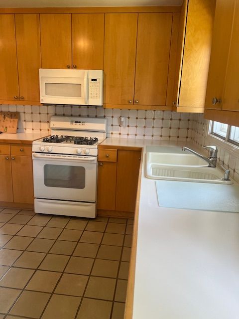 kitchen with decorative backsplash, light tile patterned floors, white appliances, and sink