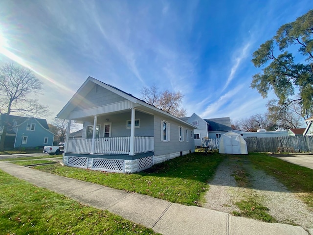 bungalow-style home featuring an outdoor structure, fence, covered porch, a front yard, and a storage shed