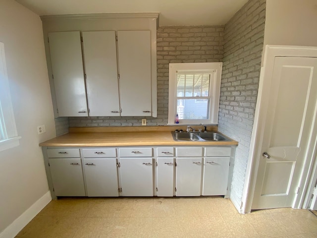 kitchen featuring white cabinetry, sink, and brick wall