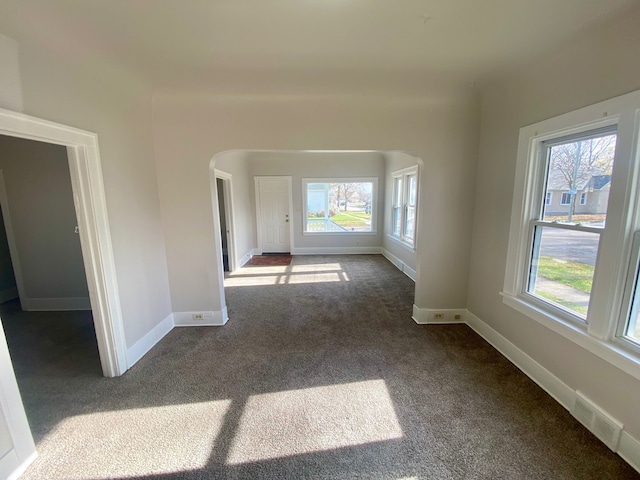 carpeted empty room with a healthy amount of sunlight, arched walkways, baseboards, and visible vents