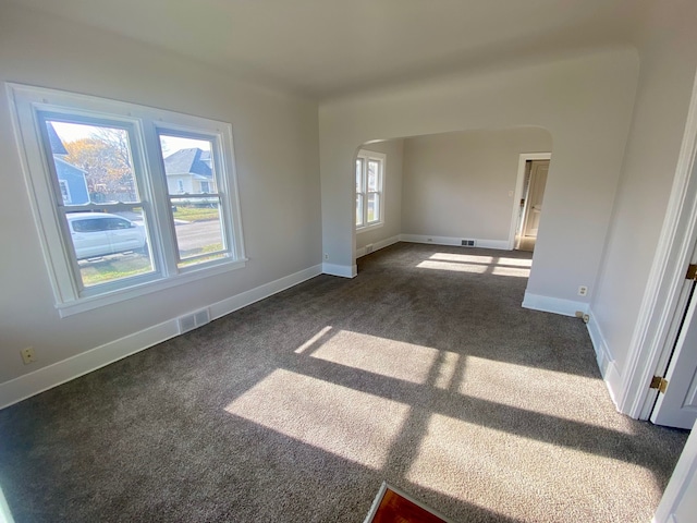 empty room featuring arched walkways, visible vents, and dark carpet