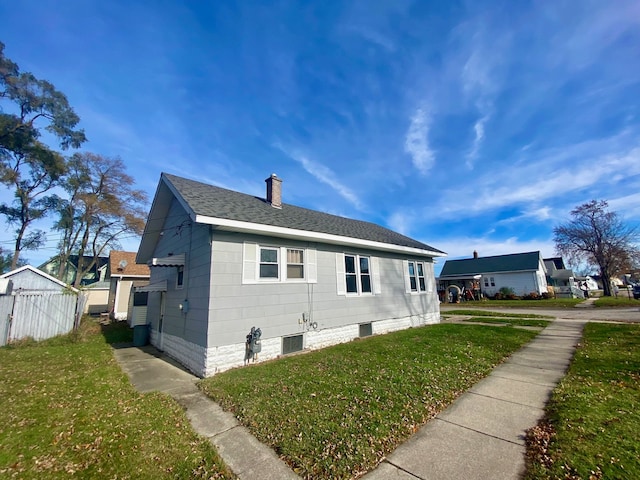 view of side of property with a shingled roof, a yard, and a chimney