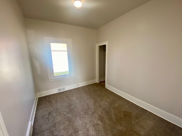 empty room featuring baseboards, visible vents, and dark carpet