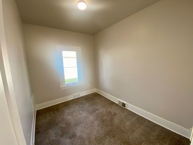 unfurnished room featuring dark colored carpet, baseboards, and visible vents