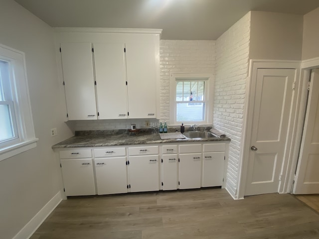 kitchen featuring white cabinets, brick wall, a sink, and light wood-style flooring