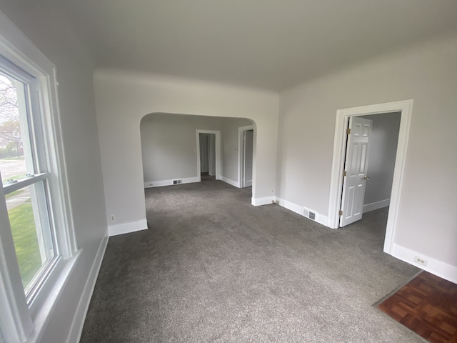unfurnished room with arched walkways, baseboards, visible vents, and dark colored carpet