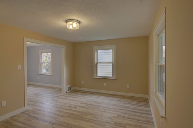 empty room with a textured ceiling and light hardwood / wood-style flooring