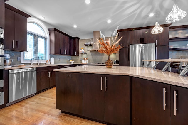 kitchen with tasteful backsplash, dark brown cabinets, ventilation hood, decorative light fixtures, and stainless steel appliances