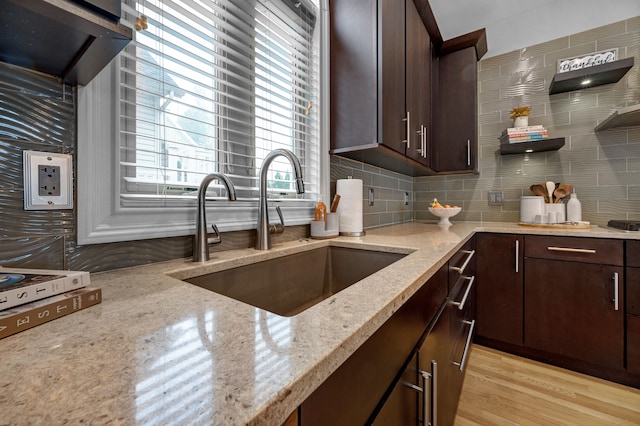 kitchen featuring light stone countertops, sink, backsplash, light hardwood / wood-style flooring, and dark brown cabinets