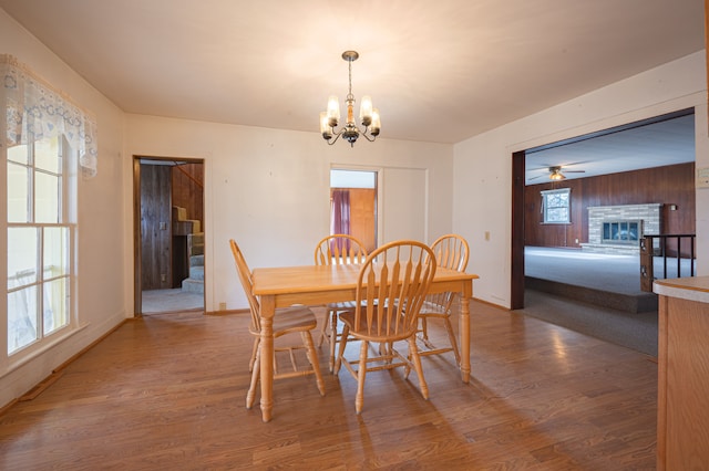 dining area featuring wooden walls, a fireplace, wood-type flooring, and ceiling fan with notable chandelier