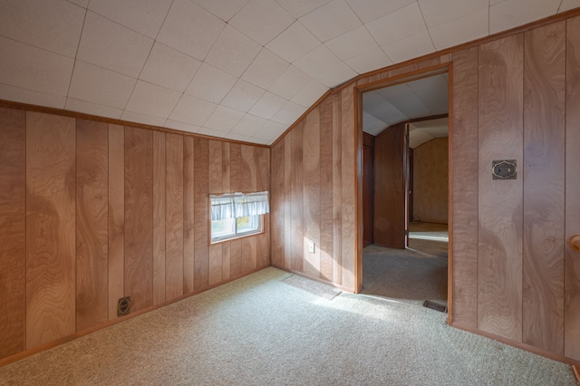 unfurnished room with carpet flooring, lofted ceiling, and wood walls