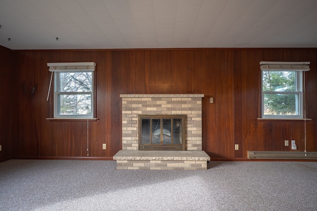 unfurnished living room with carpet flooring, wooden walls, plenty of natural light, and a brick fireplace