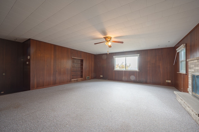 unfurnished living room with ceiling fan, wood walls, light colored carpet, and a brick fireplace