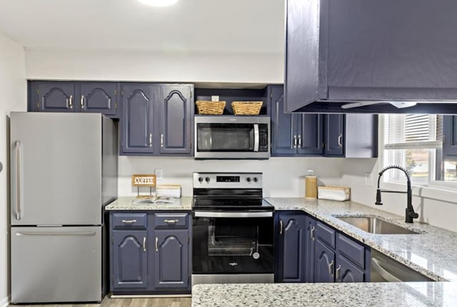 kitchen with blue cabinetry, light stone countertops, sink, stainless steel appliances, and light wood-type flooring