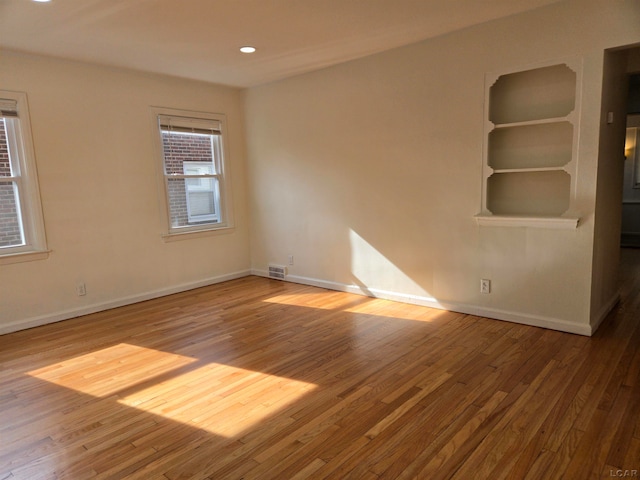 unfurnished room featuring built in shelves and hardwood / wood-style flooring