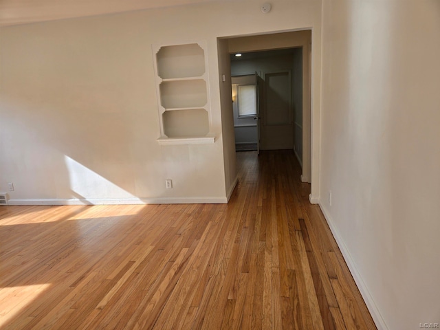 spare room with a skylight, light hardwood / wood-style flooring, and built in features