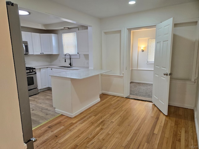 kitchen featuring kitchen peninsula, appliances with stainless steel finishes, light wood-type flooring, sink, and white cabinetry